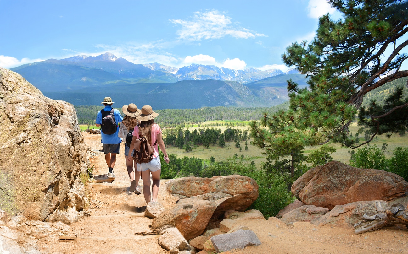 People with backpacks hiking on summer vacation in mountains. Father with his family enjoying time on a trip. Blue sky and high mountains in background. Rocky Mountain National Park, Colorado, USA.