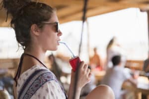 Attractive young woman relaxing on the swing at the beach bar and drinking soda.